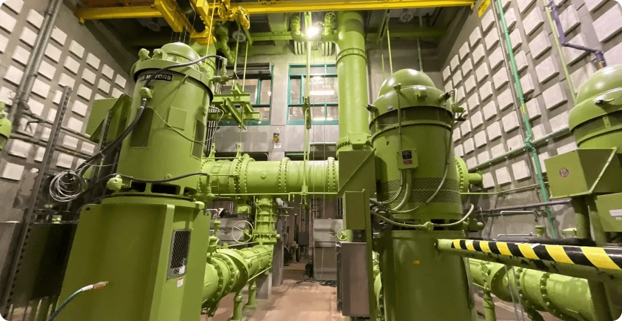 Here's an 8-word alt tag for the image: Green industrial pumps and piping in a plant.